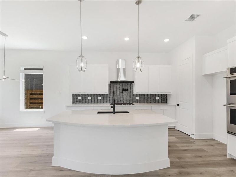Kitchen with white cabinets, backsplash, light wood-style floors, pendant lighting, and an island with sink