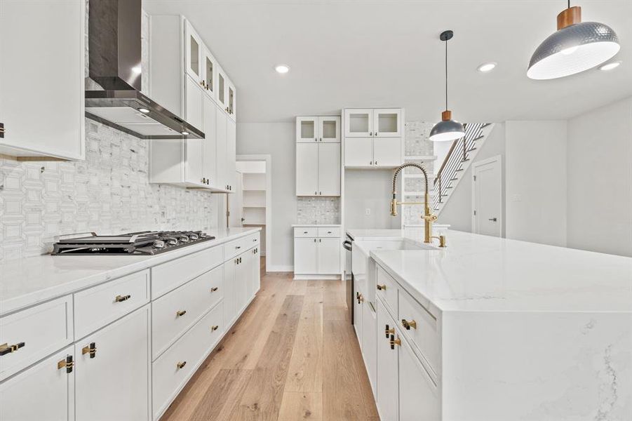 Kitchen with white cabinets, decorative backsplash, wall chimney exhaust hood, light hardwood / wood-style flooring, and a kitchen island with sink