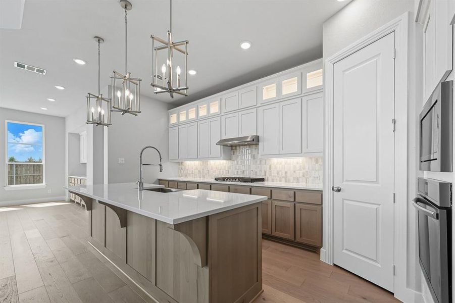 Kitchen with glass insert cabinets, an island with sink, decorative backsplash, light wood-style floors, and recessed lighting
