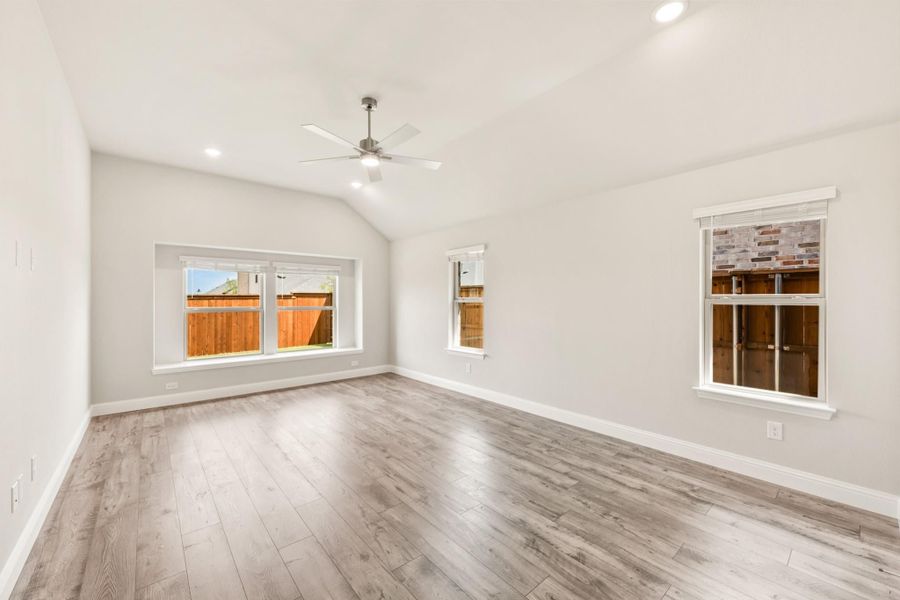 Empty room with vaulted ceiling, ceiling fan, light wood floors, and multiple windows Empty room with vaulted ceiling, ceiling fan, light wood floors, and multiple windows