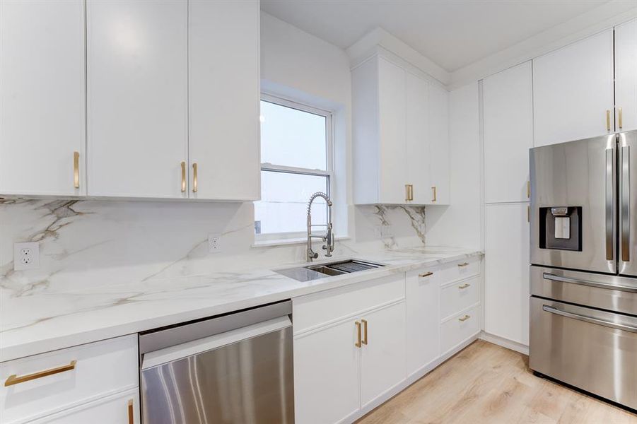 The sink area features a large window to let in natural lighting. There is a deep sink and stainless steel dishwasher.