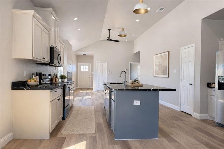 Kitchen with stainless steel appliances, a kitchen island with sink, vaulted ceiling, light wood finished floors, and a ceiling fan