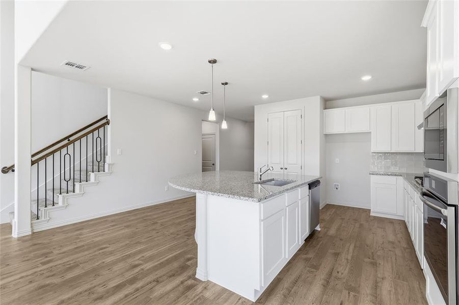 Kitchen featuring white cabinetry, light stone countertops, hanging light fixtures, a center island with sink, and recessed lighting