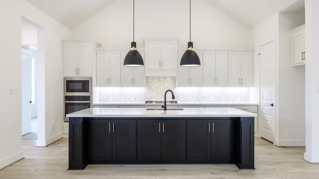 Kitchen featuring dark cabinetry, white cabinets, stainless steel oven, a kitchen island with sink, and light wood finished floors