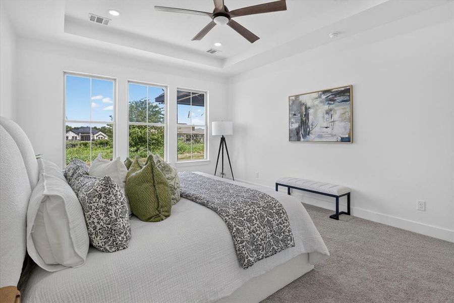 Bright room featuring three double-hung windows, a tray ceiling with a ceiling fan, and light-colored carpeting