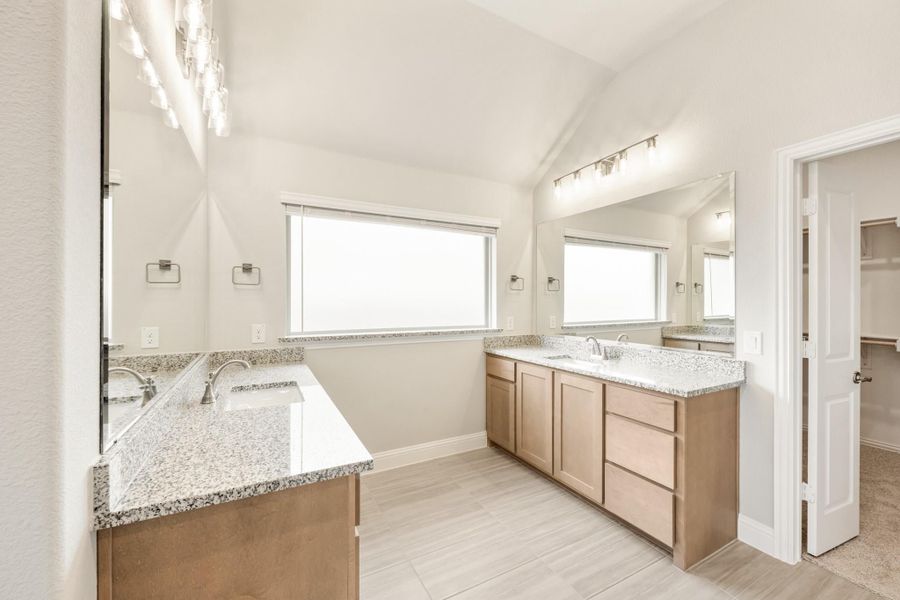 Master bathroom with dual vanities, granite countertops, vaulted ceiling, and wood-look tile floors