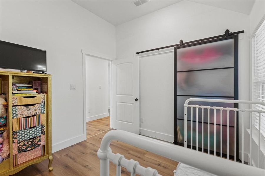 Bedroom featuring a crib, light wood-style flooring, and lofted ceiling