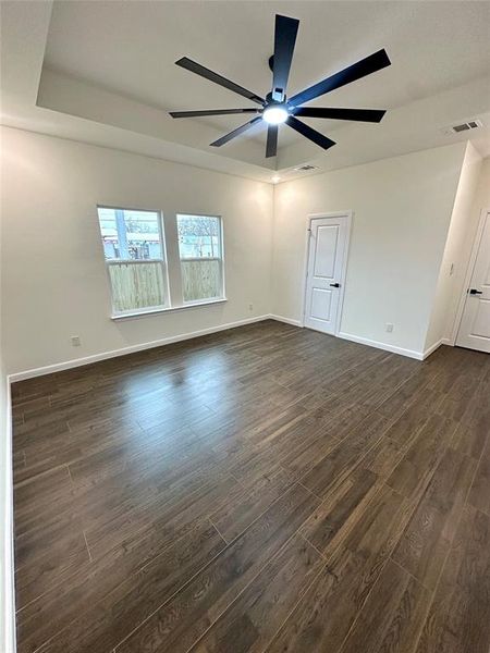 Empty room with dark hardwood / wood-style floors, ceiling fan, and a tray ceiling