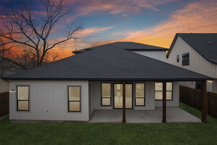 Rear view of house with a shingled roof, a fenced backyard, and a patio area