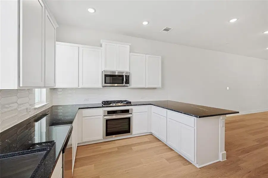 Kitchen featuring white cabinets, stainless steel appliances, light wood-style floors, and recessed lighting
