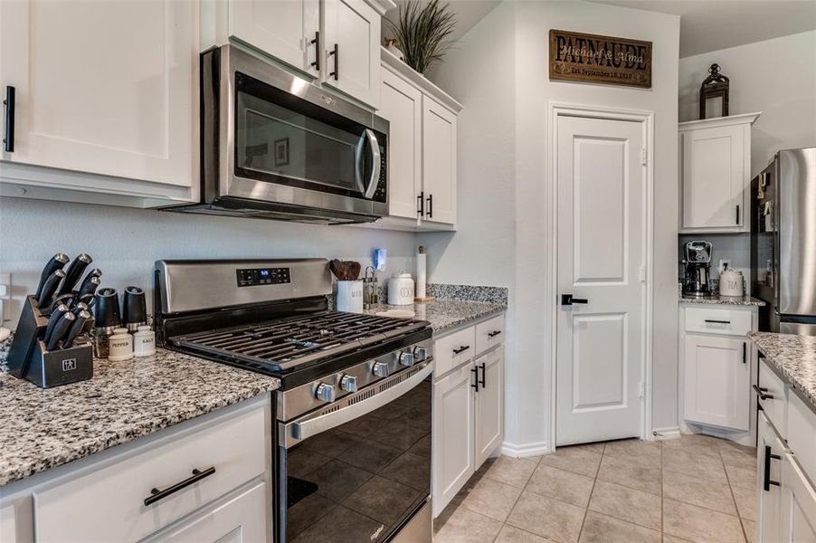 Kitchen with appliances with stainless steel finishes, white cabinetry, light tile patterned floors, and light stone countertops