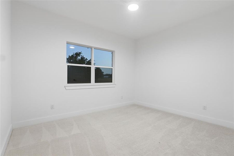 Bright room featuring a window with white trim, light-toned carpeting, white walls, and a flush-mount ceiling light
