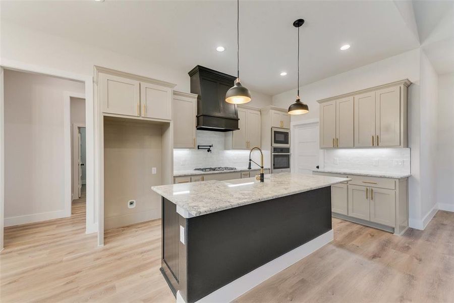 Kitchen with light stone counters, decorative backsplash, pendant lighting, an island with sink, and light wood-type flooring Kitchen with light stone counters, decorative backsplash, pendant lighting, an island with sink, and light wood-type flooring