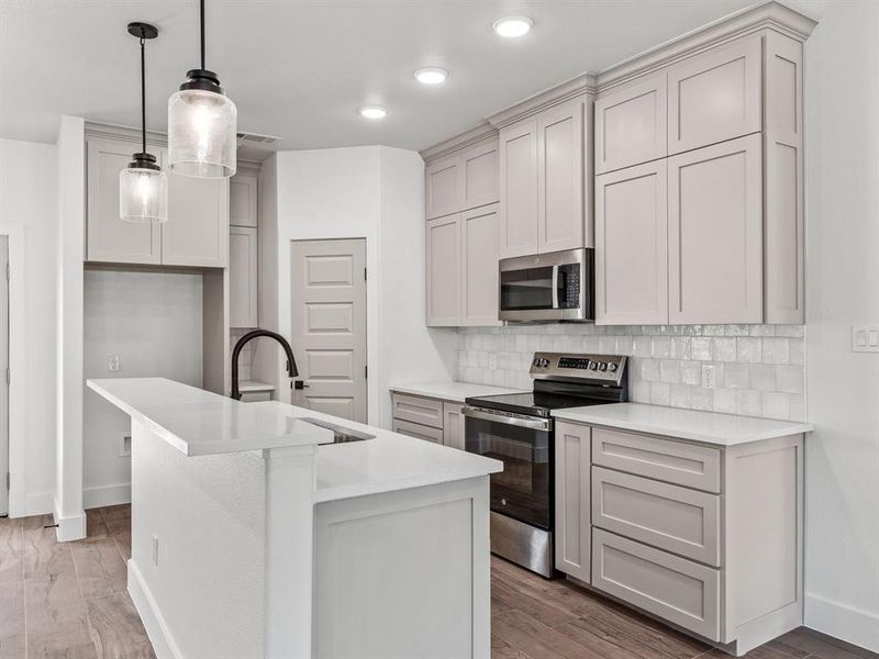 Kitchen with a kitchen island with sink, a sink, stainless steel appliances, light wood-style floors, and tasteful backsplash