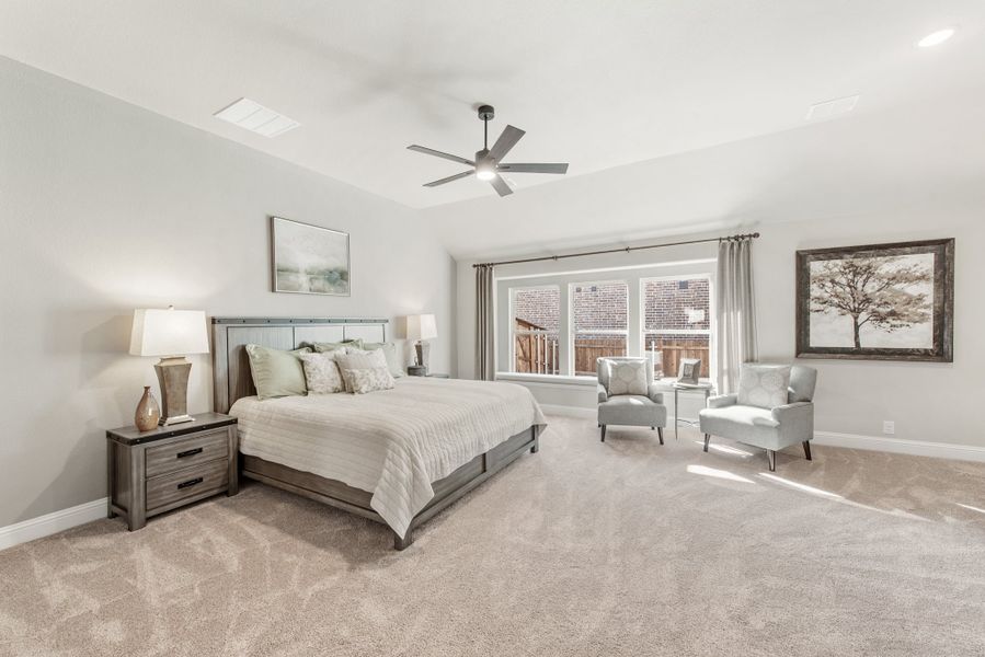 Spacious master bedroom with tray ceiling, ceiling fan, carpet floors, and a sitting area near large windows