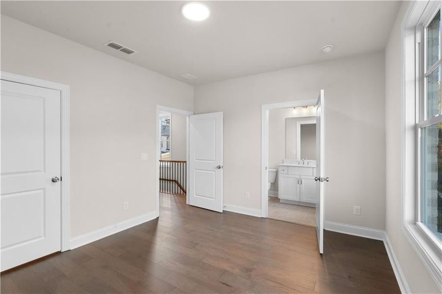 Unfurnished bedroom featuring connected bathroom and dark wood-type flooring