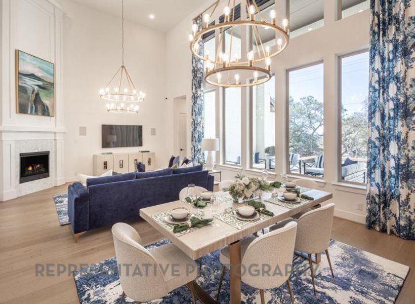 Dining space with a fireplace, a chandelier, a towering ceiling, and light wood-style floors Dining space with a fireplace, a chandelier, a towering ceiling, and light wood-style floors