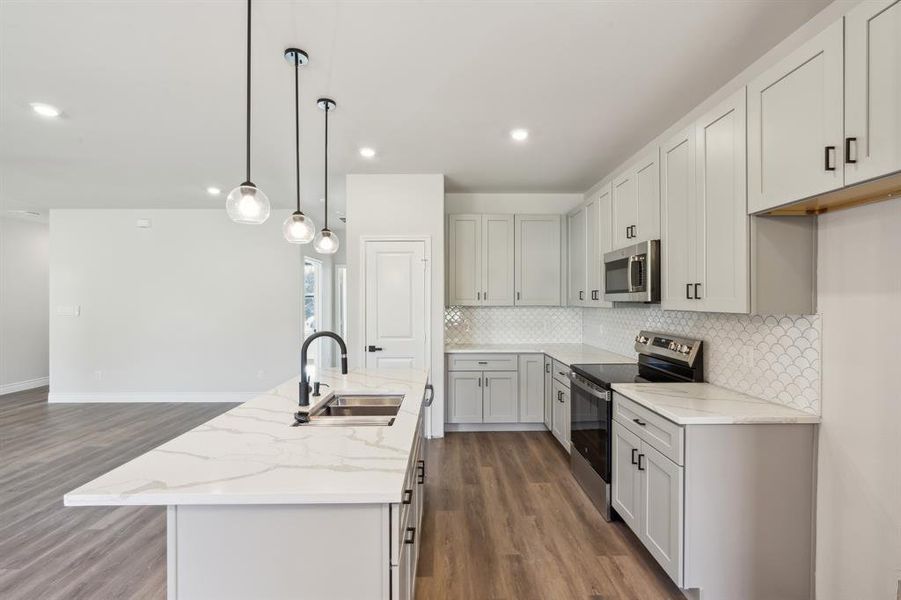 Kitchen featuring stainless steel appliances, sink, light stone counters, hanging light fixtures, and a kitchen island with sink