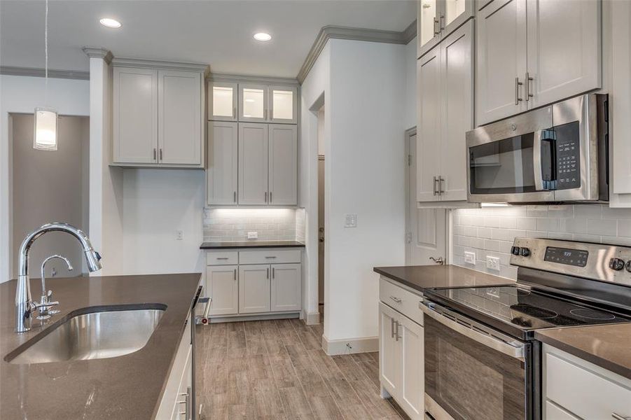 Kitchen with stainless steel appliances, glass insert cabinets, light wood-style floors, decorative light fixtures, and crown molding Kitchen with stainless steel appliances, glass insert cabinets, light wood-style floors, decorative light fixtures, and crown molding
