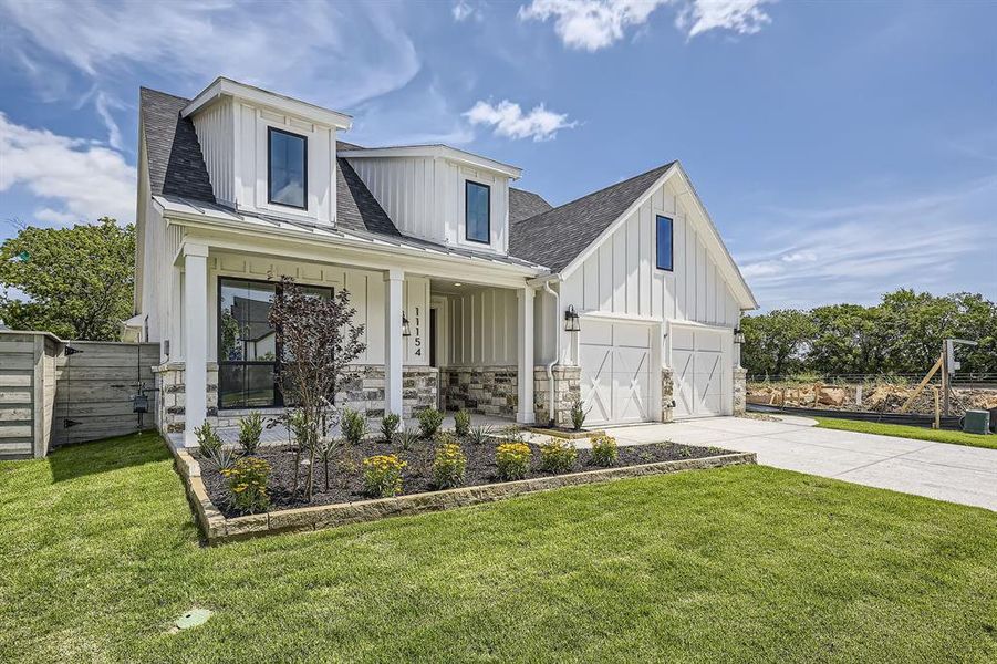 Modern farmhouse style home with board and batten siding, a porch, driveway, stone siding, and a shingled roof