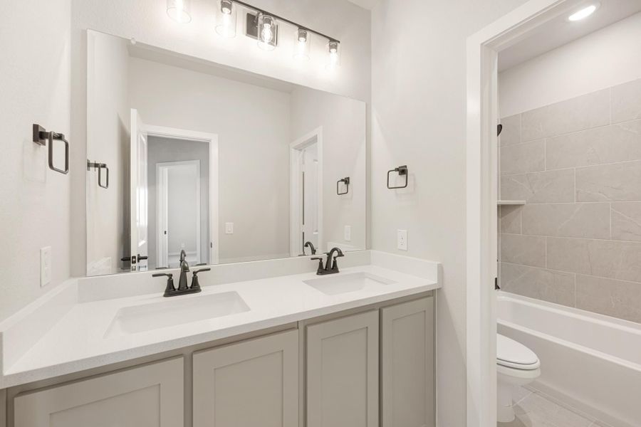Bathroom with double sink vanity, white countertop, gray cabinets, and tiled tub surround