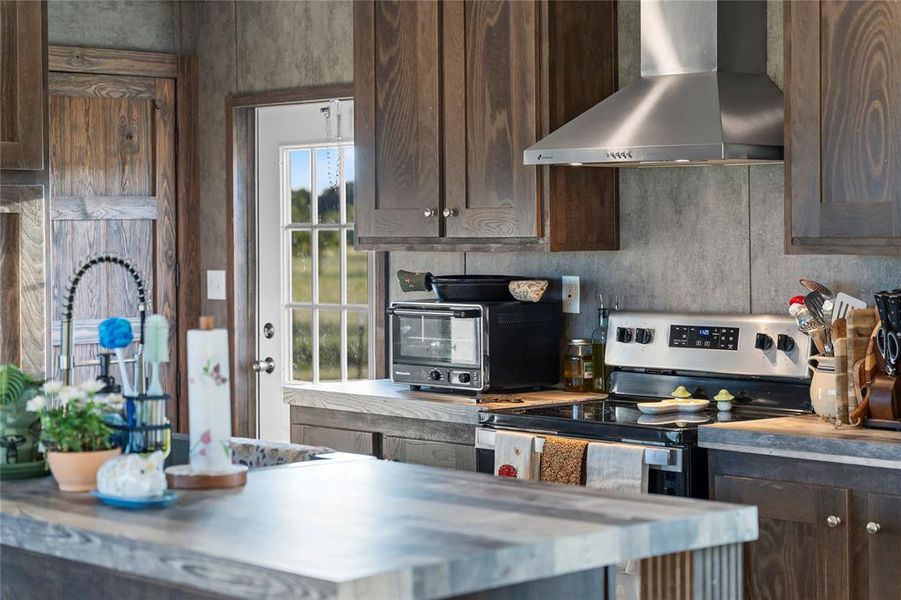 Kitchen with dark brown cabinetry, wall chimney exhaust hood, and stainless steel electric stove Kitchen with dark brown cabinetry, wall chimney exhaust hood, and stainless steel electric stove