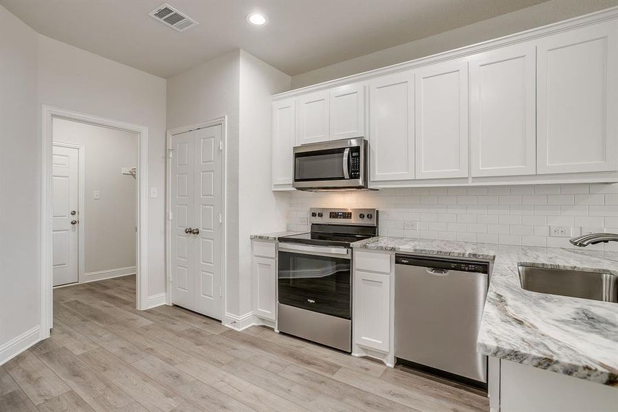 Kitchen featuring stainless steel appliances, white cabinetry, light stone counters, decorative backsplash, and light wood-type flooring