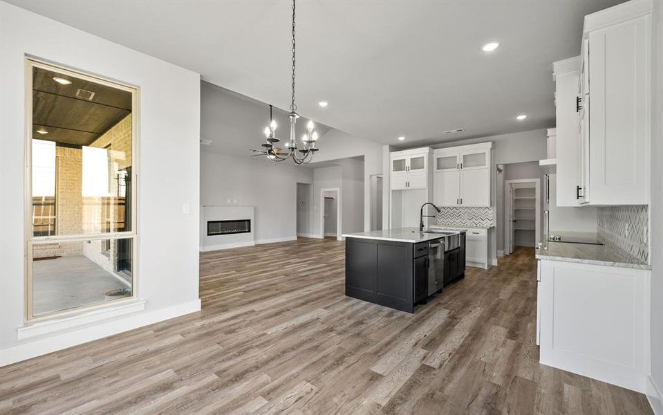 Kitchen with white cabinetry, pendant lighting, open floor plan, a glass covered fireplace, and light wood-style floors