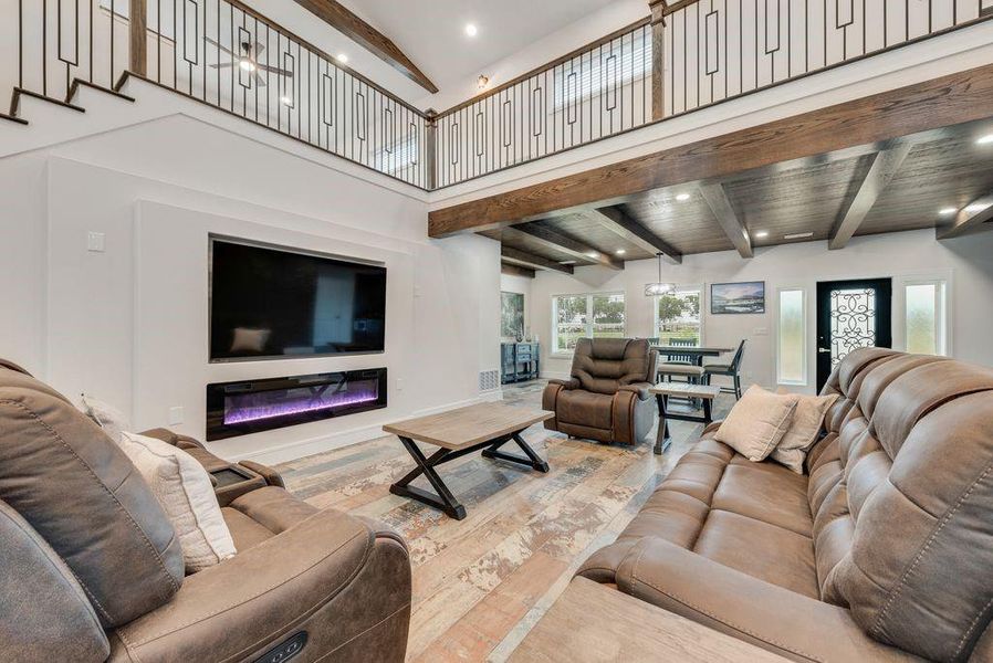 Two-story living area featuring a built-in electric fireplace and decorative wood-finish ceiling beams Two-story living area featuring a built-in electric fireplace and decorative wood-finish ceiling beams