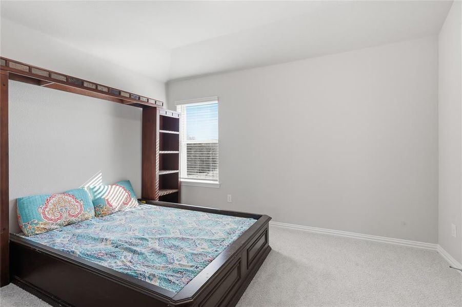 Spacious room featuring a built-in wood-finish bed frame with integrated shelving, light gray wall paint, and plush carpet flooring