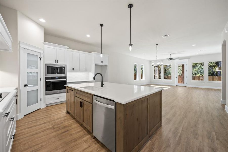Kitchen featuring white cabinets, appliances with stainless steel finishes, a center island with sink, pendant lighting, and light wood-type flooring
