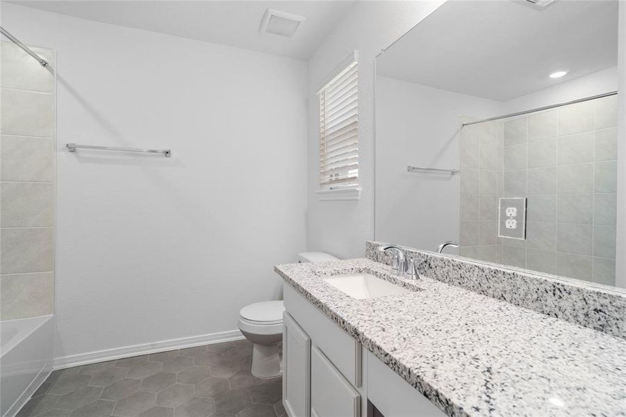 Secondary bath features tile flooring, bath/shower combo with tile surround, stained wood cabinets, beautiful granite countertops, mirror, sleek fixtures and modern finishes.