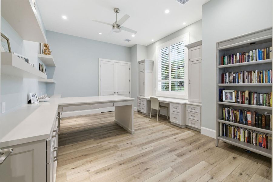 Unfurnished office with built in desk, light wood finished floors, ceiling fan, and recessed lighting
