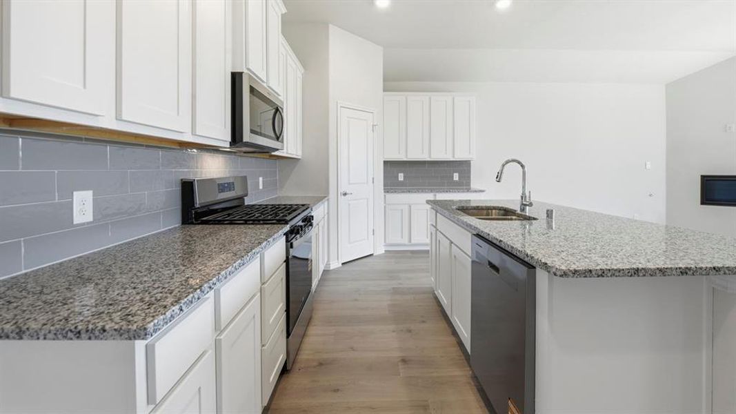 Kitchen with stainless steel appliances, light stone counters, an island with sink, white cabinetry, and light wood finished floors
