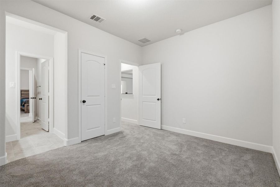 This photo shows a bright, carpeted room with neutral walls, featuring two white doors and a hallway leading to other rooms, ideal for a bedroom or office. This photo shows a bright, carpeted room with neutral walls, featuring two white doors and a hallway leading to other rooms, ideal for a bedroom or office.