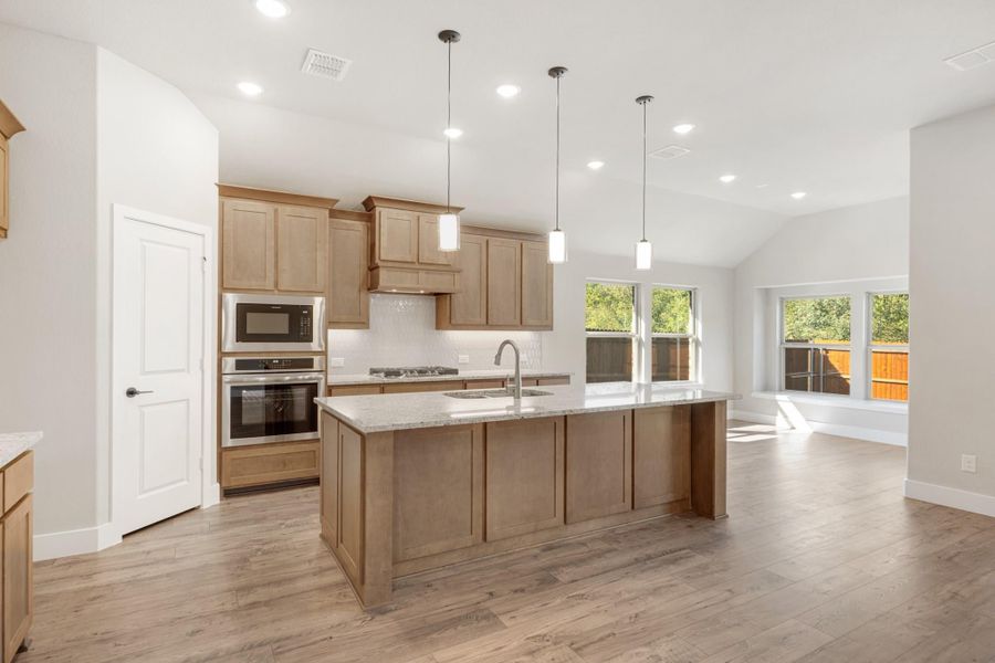 Kitchen with large center island, granite countertops, light wood cabinets, and stainless steel appliances on hardwood floors