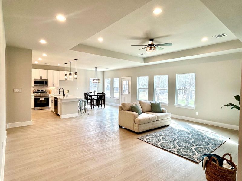 Living room featuring a raised ceiling, light wood-style floors, ceiling fan, and recessed lighting