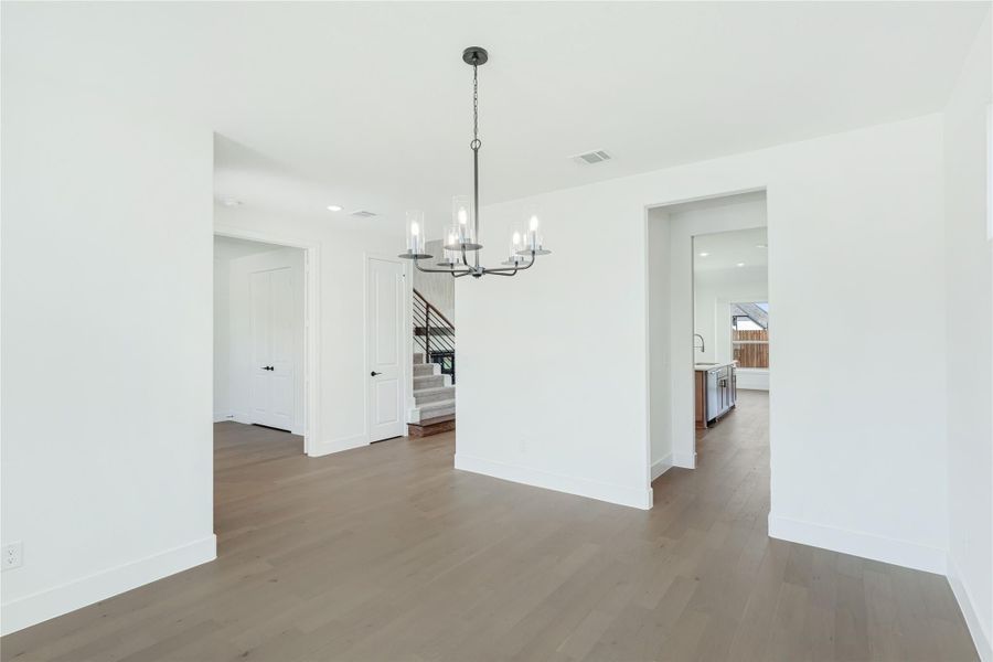 Open dining area with dark chandelier, hardwood floors, and white walls near staircase entry
