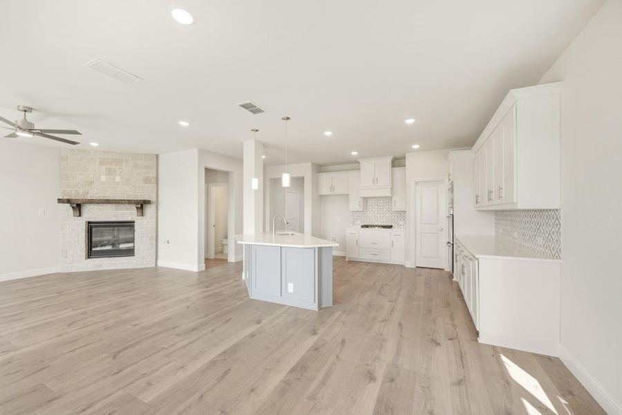 Open-concept kitchen and living area with white cabinets, center island, stone fireplace, and light wood floors