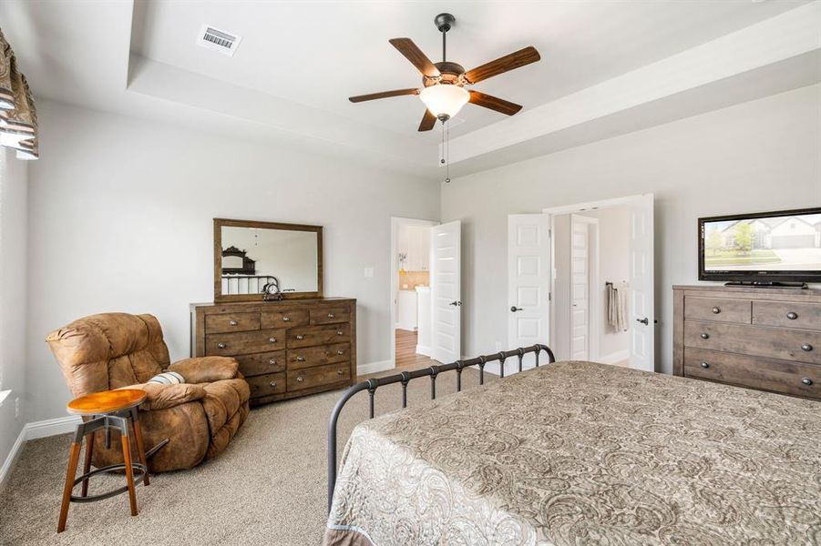 Carpeted room featuring a tray ceiling with a ceiling fan, white paneled doors, and light-colored walls Carpeted room featuring a tray ceiling with a ceiling fan, white paneled doors, and light-colored walls