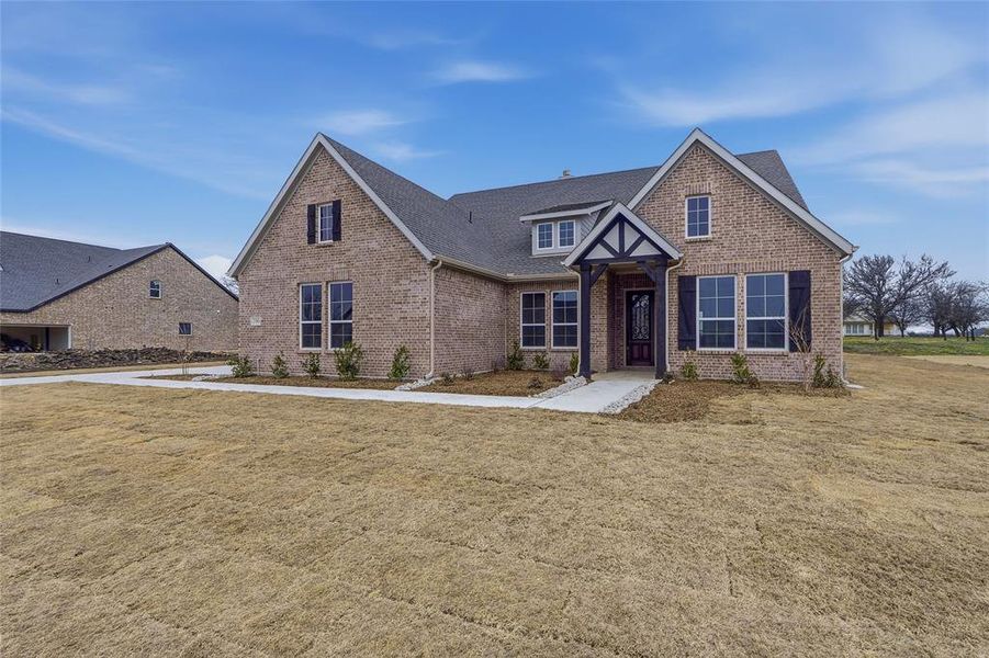 English style home featuring brick siding, a front lawn, and a shingled roof