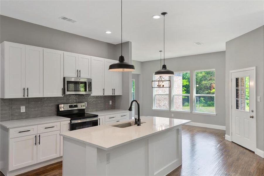 Kitchen featuring sink, hanging light fixtures, stainless steel appliances, and a kitchen island with sink