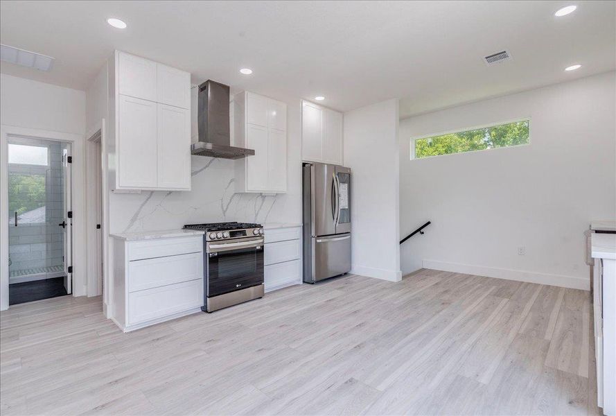 Kitchen featuring appliances with stainless steel finishes, range hood, light wood-type flooring, white cabinetry, and recessed lighting