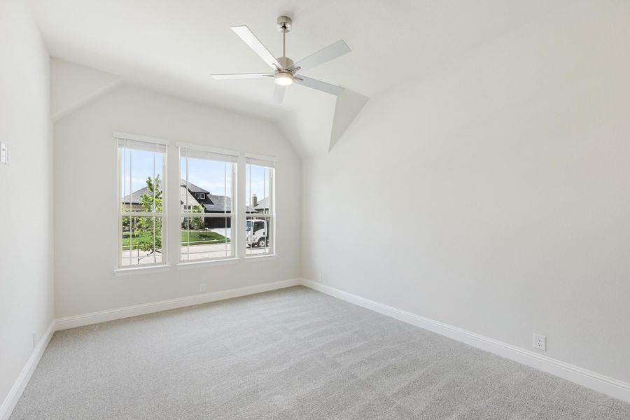 Empty bedroom with vaulted ceiling, ceiling fan, gray carpet, and triple window with neighborhood view Empty bedroom with vaulted ceiling, ceiling fan, gray carpet, and triple window with neighborhood view