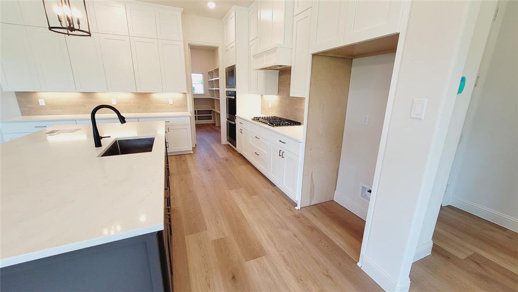 Gourmet kitchen featuring a large island with an undermount sink, white cabinetry with under-cabinet lighting, a gas cooktop, double wall ovens, and wood-finish flooring