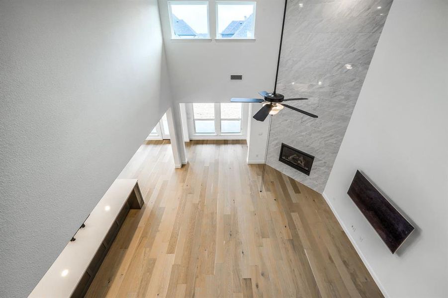 Unfurnished living room featuring visible vents, light wood finished floors, a high ceiling, ceiling fan, and a tiled fireplace