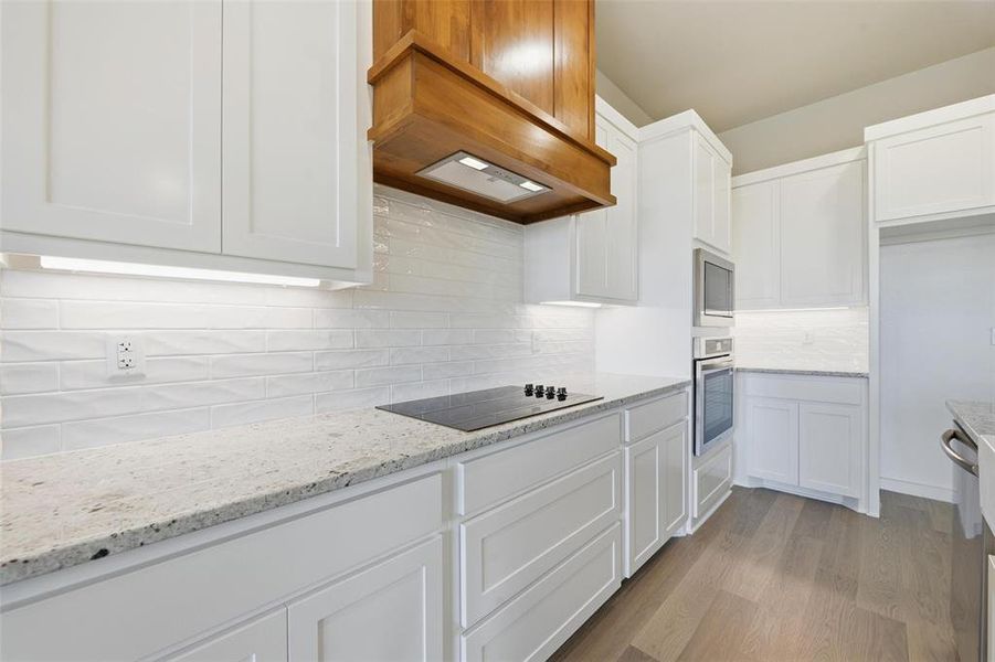 Kitchen featuring white cabinets, light wood-style floors, light stone countertops, decorative backsplash, and stainless steel appliances