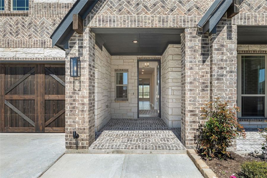 Covered brick entryway with stone columns, wood garage door, and wall sconce light fixture