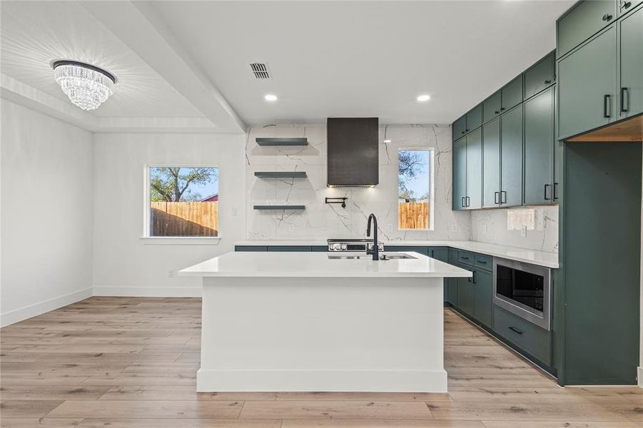 Kitchen with green cabinetry, tasteful backsplash, open shelves, an island with sink, and recessed lighting