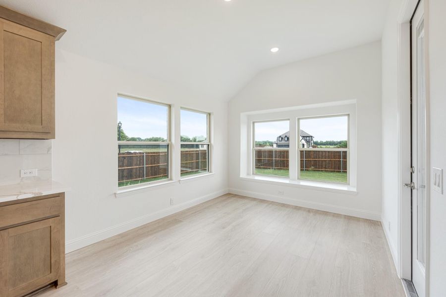 Empty dining nook with vaulted ceiling, light wood floors, and three windows overlooking backyard fence Empty dining nook with vaulted ceiling, light wood floors, and three windows overlooking backyard fence